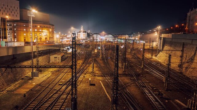 Night timelapse of main historic railway station with dynamic train movement and light trails across multiple tracks. Urban european transport, travel city infrastructure.