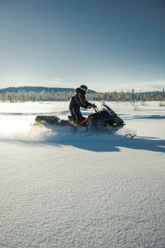 Side view of person driving snowmobile on snowy field against sky