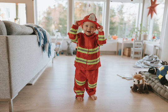 Cute boy dressed in firefighter costume standing at home