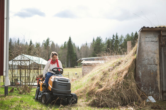 Woman driving lawn tractor near stack of grass in farm