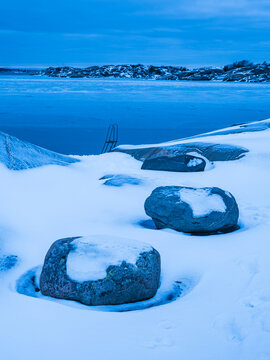 Shot of large rocks in deep white snow near frozen lake