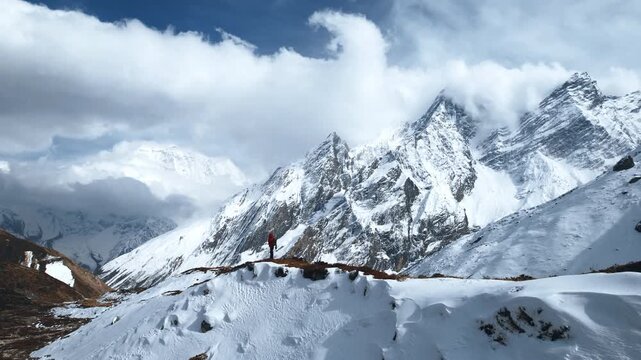 Stunning footage of a lone trekker on a snowy ridge gazing at towering Himalayan peaks shrouded in dramatic billowing clouds in Nepal's Manaslu region.