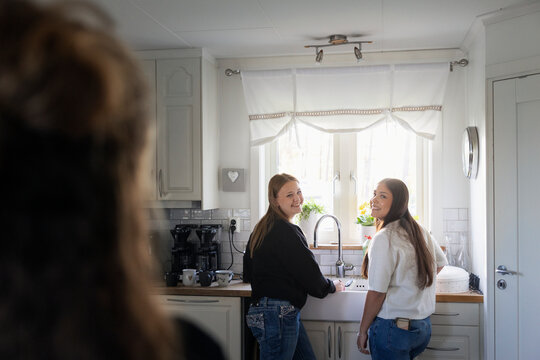 Smiling teenage girl looking over shoulder while standing near kitchen sink at home