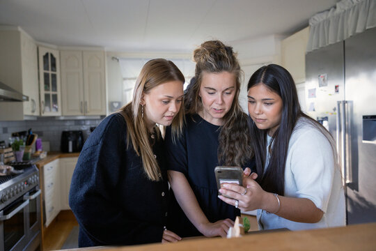 Long haired teenage girl showing smart phone to friend and her mother at home