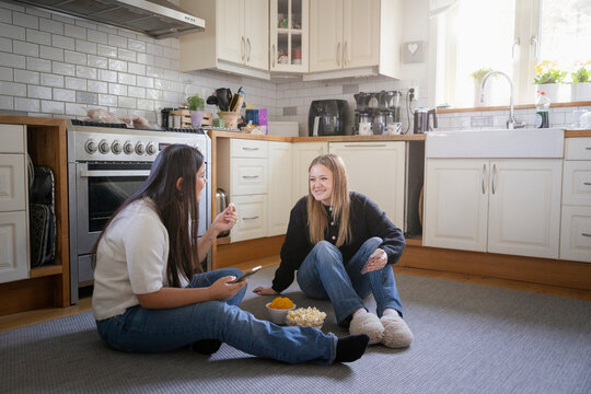 Happy multiracial female friends spending leisure time while sitting on kitchen floor at home