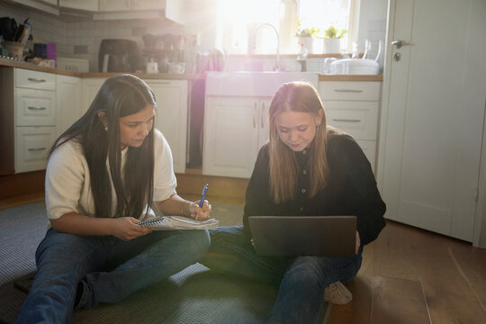Multiracial female friends doing homework while sitting on kitchen floor at home
