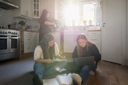 Focused teenage girls doing homework while sitting on kitchen floor at home