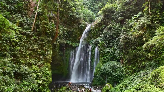 Aerial view of Tiu Kelep Waterfall with cascading water surrounded by lush tropical forest and people at the base Bayan, West Nusa Tenggara, Indonesia.