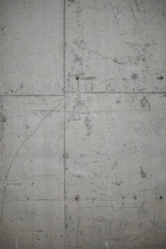Close-up full-frame shot of a weathered gray exposed concrete wall. Features visible construction panel seams, tie-rod holes, surface scratches, and a raw industrial texture ideal for architectural 