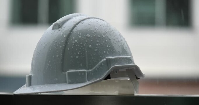 Raindrops on a white helmet against a backdrop of a construction site in the rain; rainy season and construction.	