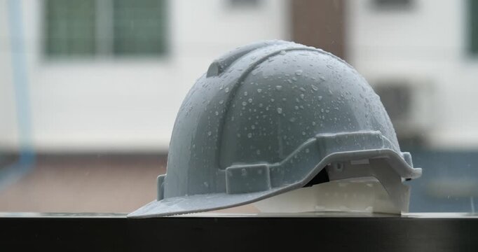 Raindrops on a white helmet against a backdrop of a construction site in the rain; rainy season and construction.	