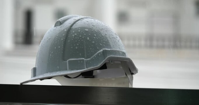 Raindrops on a white helmet against a backdrop of a construction site in the rain; rainy season and construction.	