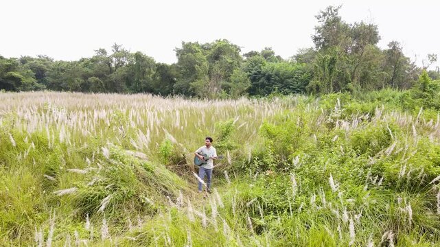 Young singer singing and playing guitar in kans grass field in Bangladesh