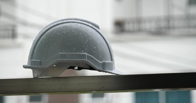 Raindrops on a white helmet against a backdrop of a construction site in the rain; rainy season and construction.