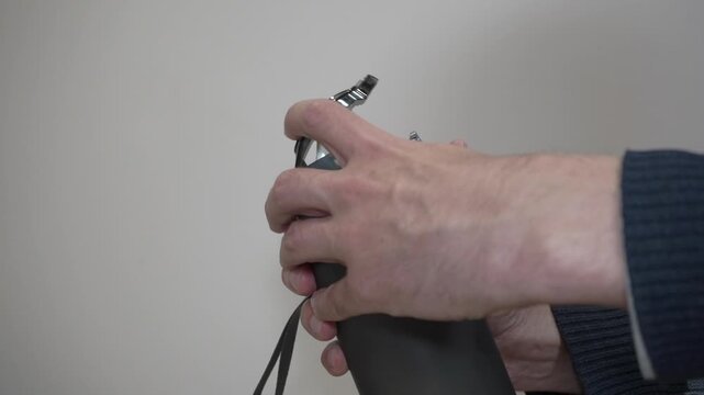 Hand opening the protective lid of a reusable sports water bottle, Close-up of person opening flip-top cap on a dark grey plastic bottle.