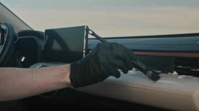 A gloved hand cleans the leather console with a special brush and chemicals inside the car. Gently