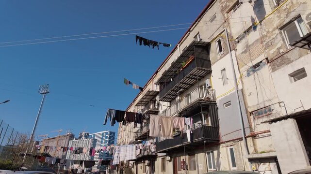 Low-angle view of laundry drying on clotheslines strung between old, weathered apartment buildings in a poor neighborhood, showing a stark contrast with modern skyscrapers in the distance