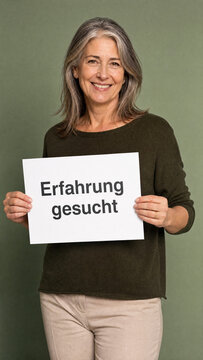 L&auml;chelnde Frau Anfang 50 mit grauen Haaren h&auml;lt wei&szlig;es Schild Erfahrung gesucht vor Sage Green Studio &ndash; Senior Recruiting Mature Workforce