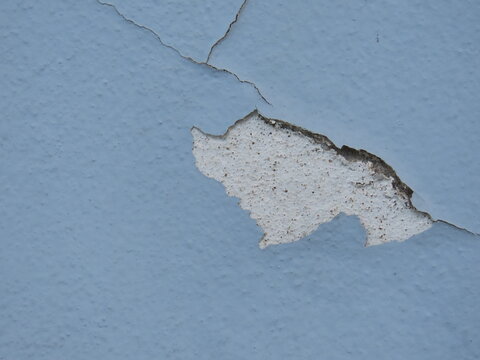 Closeup of a weathered light blue wall with flaking paint. Closeup of wall with cracked paint.