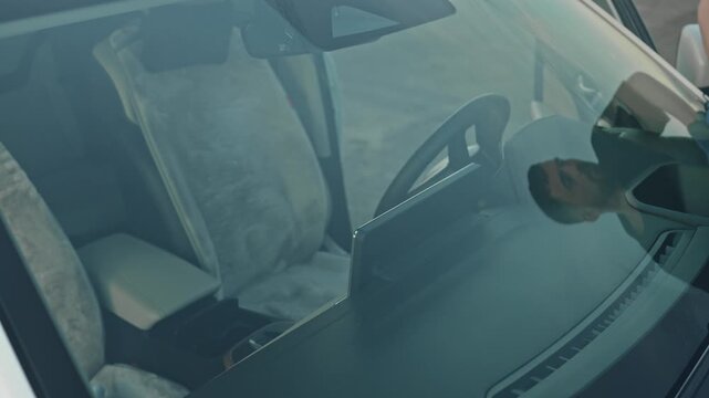 A white man wipes the windshield from the outside, and reaches across the cabin for a microfiber cloth to remove the streaks. He's wearing gloves on his hands