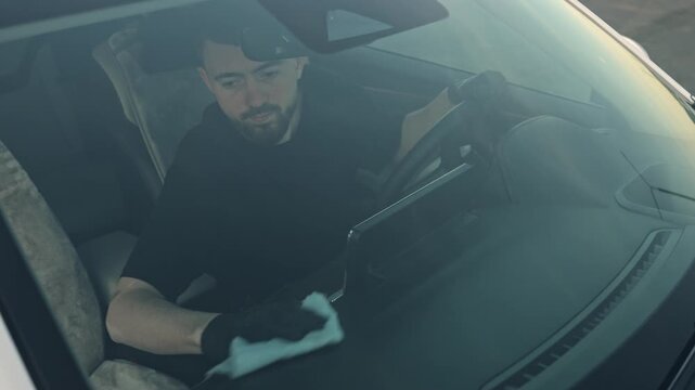 Caucasian Man inspects the car interior, then wipes it, lifts the fabric to check its cleanliness, and carefully examines it from different angles in the soft afternoon light.