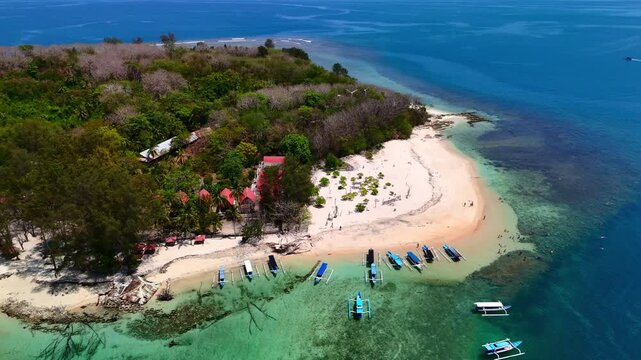 Aerial view of Gili Nanggu island featuring a white sand beach and outrigger boats anchored in turquoise water in Sekotong, West Nusa Tenggara, Indonesia.