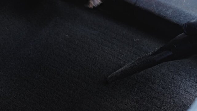 Dark Car Carpet Being Vacuumed By Gloved Hand, Closeup Nozzle And Brush Work Across Footwell Mat Lifting Dirt