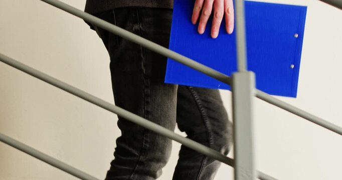 Businessman in elegant blazer walks down concrete staircase carrying detailed report. Man descends staircase carrying official documents with careful attention