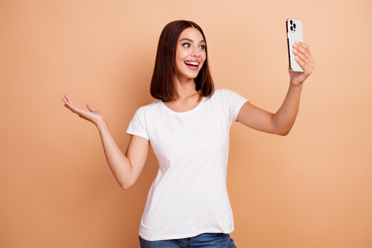 Young woman taking a cheerful selfie in a white tshirt against a beige background