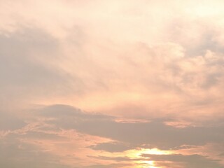 Obraz premium A serene and beautiful sunset sky filled with soft pastel orange and peach colored clouds. The gentle sun glows from the horizon, creating a peaceful, warm, and dreamy atmospheric background