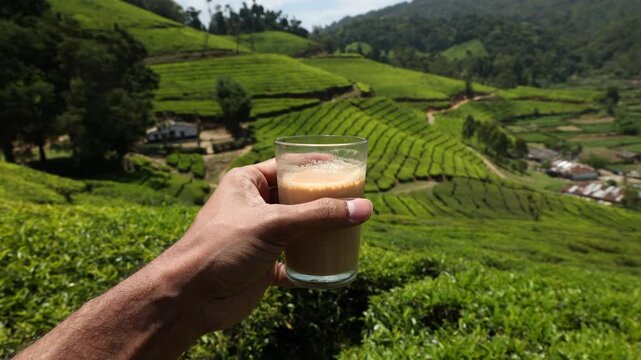 Man hand holding drinking a glass of  tea in front of  Tea Plantation Munnar, Kerala, India. breathtakingly beautiful haven of peace and tranquility idyllic tourist destination in Kerala India