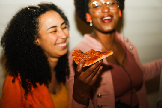 African american girls eating pizza outdoor in the streets after party concert - Food, people lifestyle and nightlife concept - Main focus on afro woman hand - UGC flash content