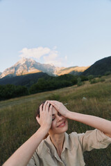 Fototapeta premium Cheerful woman outdoors, enjoying sunlight, relaxed pose, hands on head, smiling expression, natural colors, wide field scenery, distant mountains, calm breeze