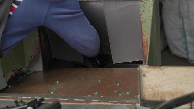 Worker in blue uniform operates machinery with plastic pellets on metal conveyor belt in factory