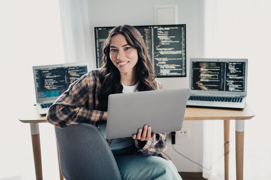 Smiling woman programmer working on laptop with multiple monitors showing code in a bright home office, remote developer coding software and studying projects on computers