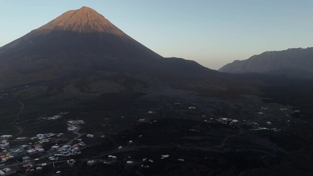 Aerial view of the Ch&atilde; das Caldeiras village at the base of the majestic Pico do Fogo volcano in Cabo Verde, surrounded by vast, ancient volcanic lava flows during golden hour
