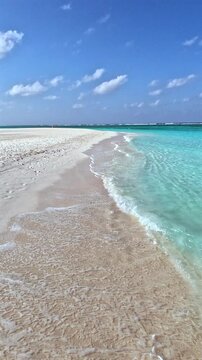 Tropical Beach Scene with Turquoise Water and White Sand. Tropical white sand beach with gentle turquoise ocean waves under blue sky with clouds. Relaxing exotic paradise destination ideal for travel.