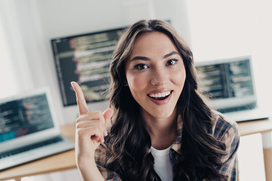Smiling woman programmer pointing up while coding at home office with multiple laptops and code on screens, remote developer working on software and web development