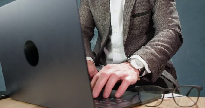Male masked scammer shows rubber rooster near laptop after online fraud message. Man presents toy as mockery continuing deceptive communication at coffee table