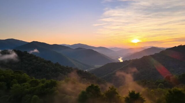 Sunrise over misty mountain valley bathed in golden light, aerial perspective reveals rolling ridges, lowlying fog, forested slopes and distant river reflecting sun, pastel sky with wispy clouds,