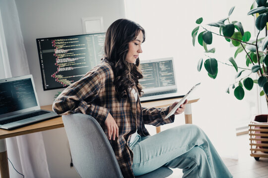 Woman programmer working from home office with laptop and tablet, coding and reviewing computer code in a modern remote workspace