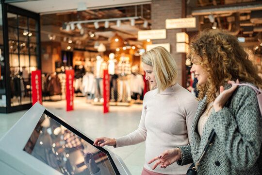 Women using interactive touch screen kiosk in shopping mall