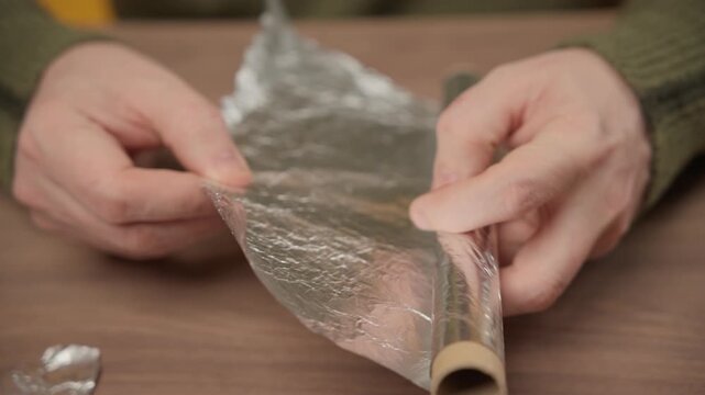 Person tearing or preparing silver tin foil for cooking or food storage on a wooden table