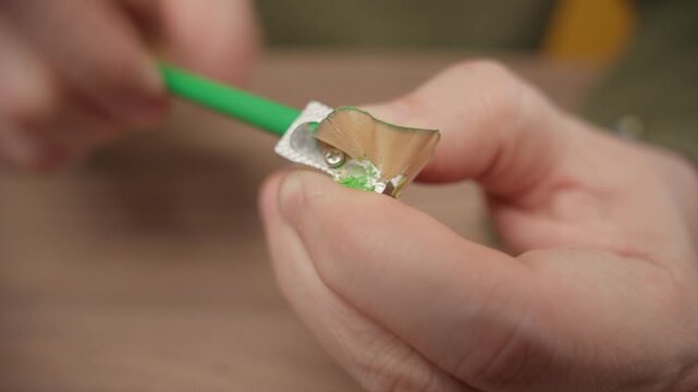 Close-up of hands sharpening a green pencil with a small silver metal sharpener.