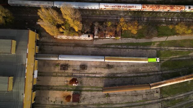 Aerial view of a railway maintenance depot with several passenger train carriages parked on parallel tracks beside a large workshop building, showing rail infrastructure, rolling stock and servicing f