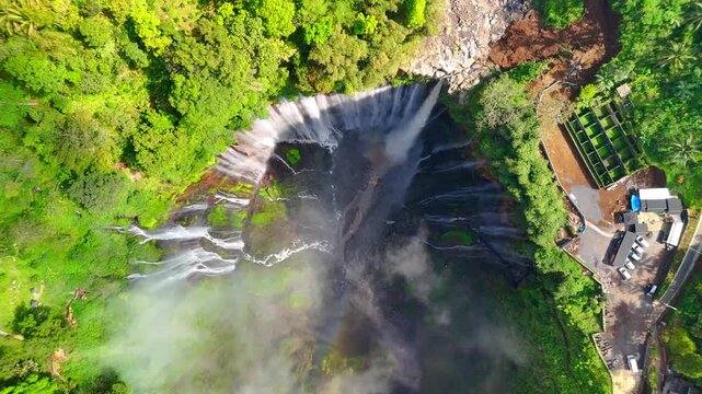 Aerial view of Tumpak Sewu Waterfall cascading into a deep canyon surrounded by lush tropical jungle and mist in Kecamatan Pronojiwo, Jawa Timur, Indonesia.