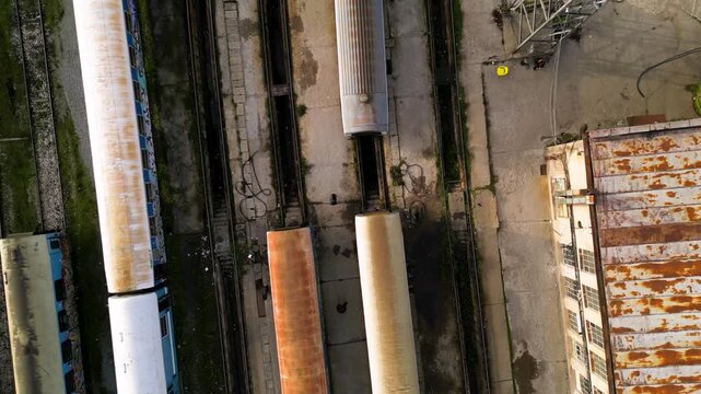 Aerial view of a railway maintenance depot with several passenger train carriages parked on parallel tracks beside a large workshop building, showing rail infrastructure, rolling stock and servicing f