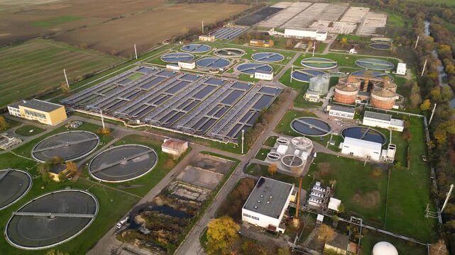 High-altitude drone perspective of an agricultural-edge sewage processing installation featuring dense arrays of round sedimentation tanks, long settling pools, support buildings, and open farmland su