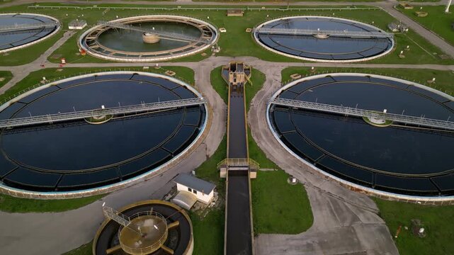 Aerial view of a wastewater treatment plant with multiple large circular clarifier tanks, sedimentation basins, channels and filtration structures arranged in a geometric industrial water-processing c