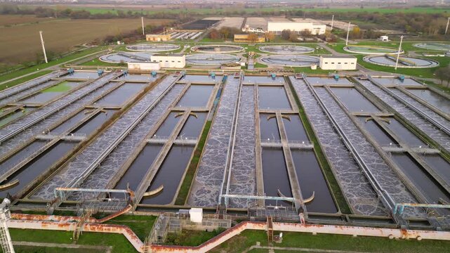 Aerial view of a wastewater treatment plant with multiple large circular clarifier tanks, sedimentation basins, channels and filtration structures arranged in a geometric industrial water-processing c